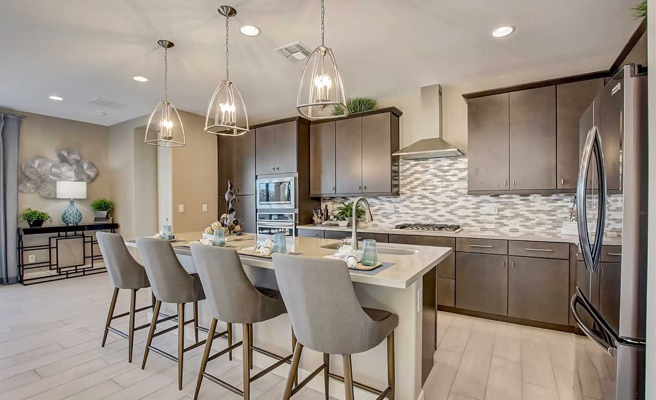 Elegant Kitchen Design in The Lakes at Rancho El Dorado Community Modern kitchen with dark cabinets, island, pendant lights, and backsplash at The Lakes at Rancho El Dorado community.