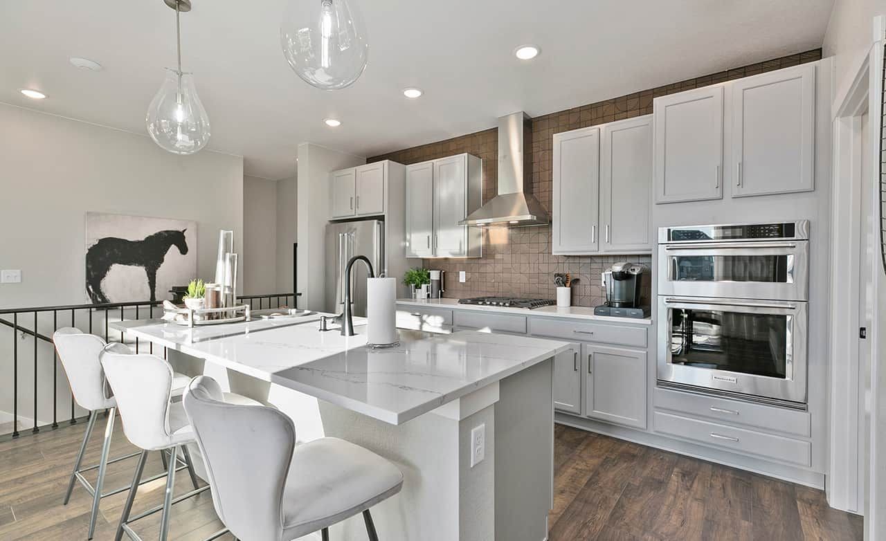 Luxurious Kitchen with Marble Island in Trailside on Harmony Modern kitchen with marble island, pendant lights, stainless steel appliances, and wall art in Trailside on Harmony.